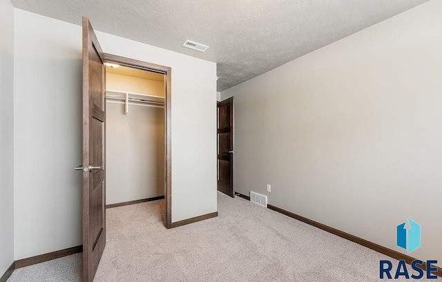 unfurnished bedroom with light carpet, a textured ceiling, visible vents, and baseboards