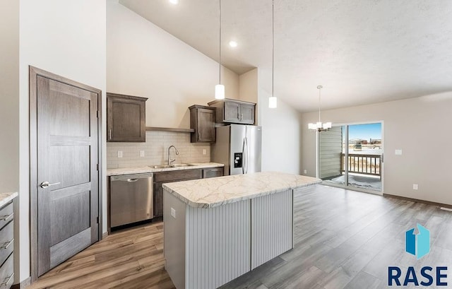 kitchen featuring dark wood-style floors, a center island, stainless steel appliances, hanging light fixtures, and a sink