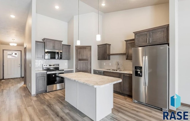 kitchen featuring stainless steel appliances, a sink, hanging light fixtures, dark brown cabinets, and a center island