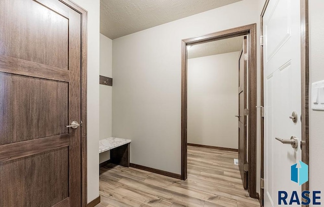 mudroom with light wood-style floors, baseboards, and a textured ceiling