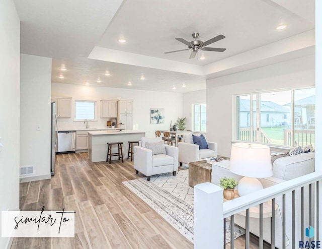 living area with visible vents, a tray ceiling, light wood-style flooring, and recessed lighting