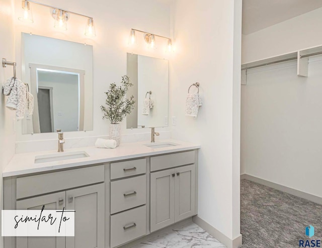 full bathroom with double vanity, marble finish floor, a walk in closet, and a sink