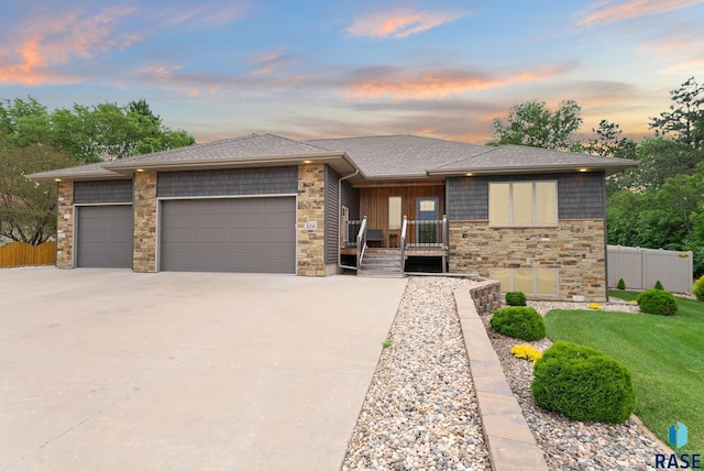 prairie-style home featuring an attached garage, stone siding, fence, and concrete driveway