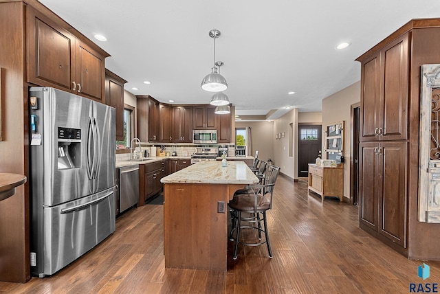 kitchen featuring light stone counters, stainless steel appliances, a sink, a kitchen island, and pendant lighting