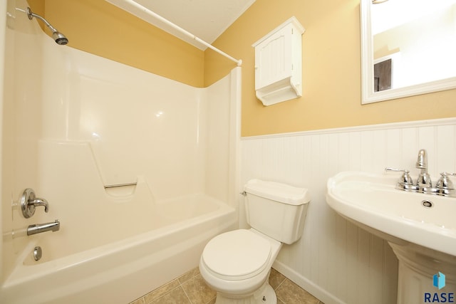 full bath featuring toilet, a wainscoted wall, shower / bath combination, a sink, and tile patterned floors