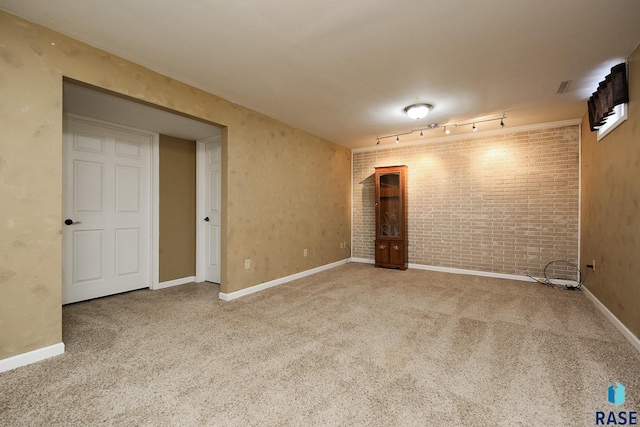 carpeted empty room featuring baseboards, brick wall, and track lighting