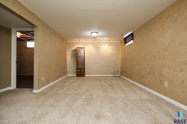 below grade area with carpet floors, rail lighting, brick wall, and baseboards