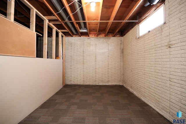 basement featuring brick wall and dark carpet