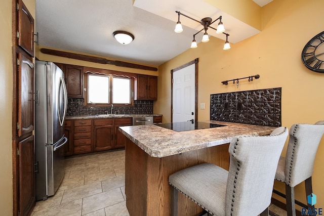 kitchen featuring a peninsula, stainless steel appliances, a sink, a kitchen breakfast bar, and backsplash