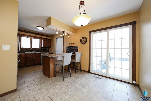 kitchen featuring a breakfast bar, decorative light fixtures, dark countertops, decorative backsplash, and a peninsula