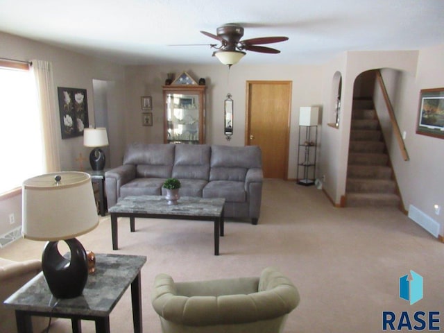 living room featuring light carpet, stairs, and a ceiling fan