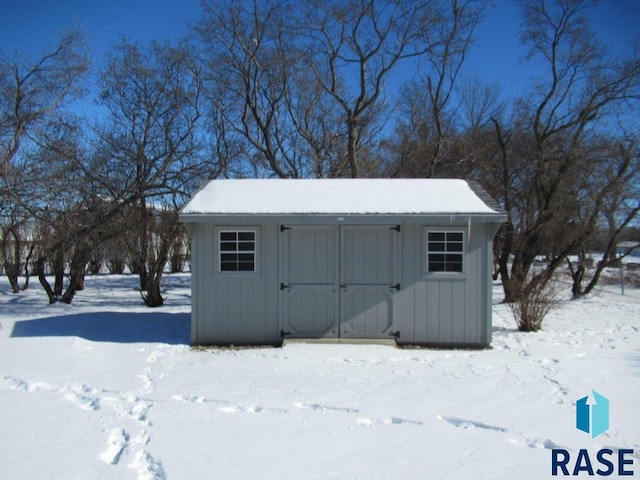 snow covered structure featuring an outbuilding and a shed