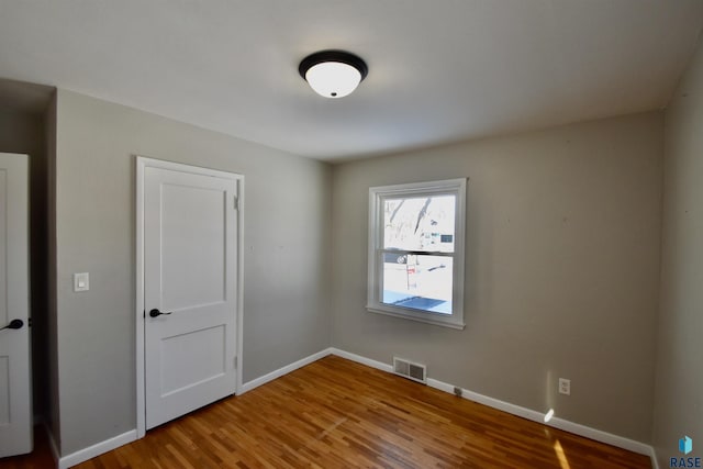 spare room featuring wood finished floors, visible vents, and baseboards