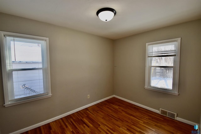 spare room with wood finished floors, visible vents, and baseboards