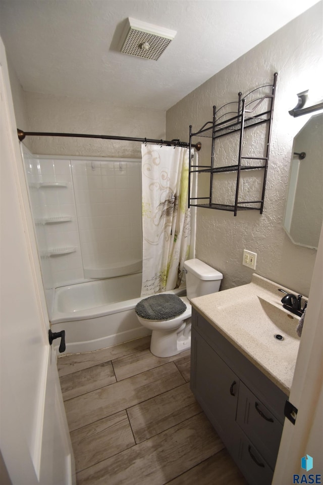 bathroom with a textured wall, toilet, wood finished floors, vanity, and visible vents