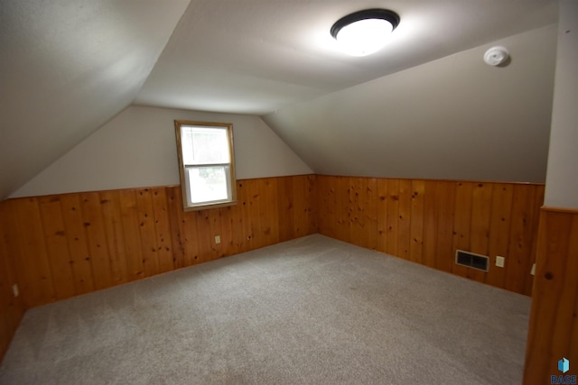 additional living space featuring lofted ceiling, wood walls, visible vents, and carpet flooring