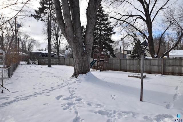 yard covered in snow with a playground and a fenced backyard