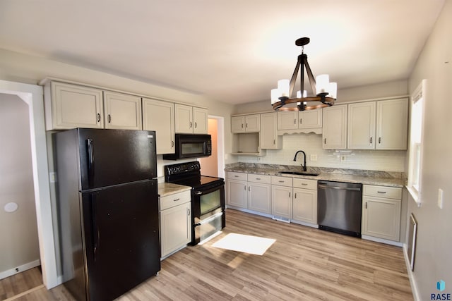 kitchen with a sink, decorative backsplash, black appliances, light wood finished floors, and decorative light fixtures