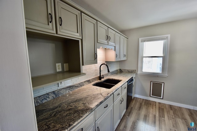 kitchen featuring black dishwasher, tasteful backsplash, stone countertops, a sink, and light wood-type flooring