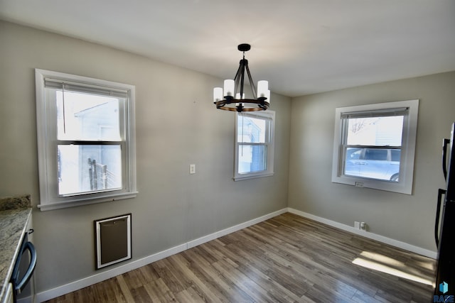 unfurnished dining area with an inviting chandelier, baseboards, and wood finished floors