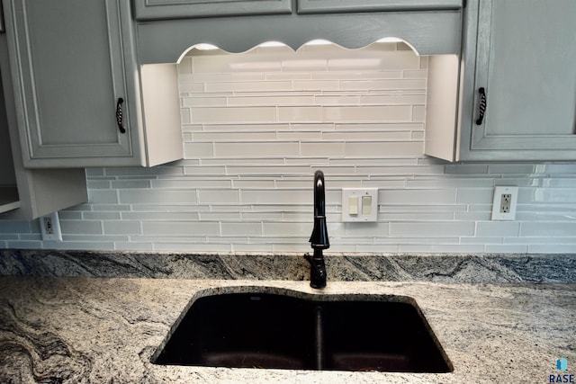 details featuring gray cabinets, stone counters, a sink, and tasteful backsplash