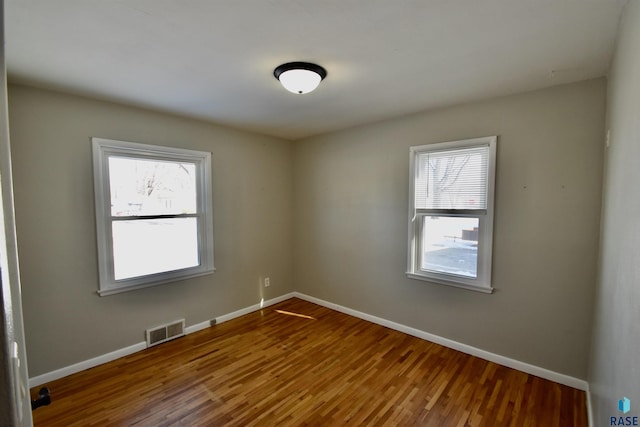 unfurnished room with wood finished floors, visible vents, and baseboards