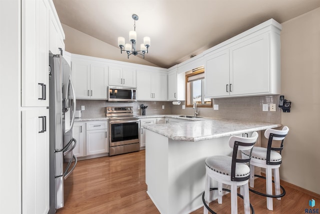 kitchen featuring white cabinets, a peninsula, stainless steel appliances, pendant lighting, and a sink