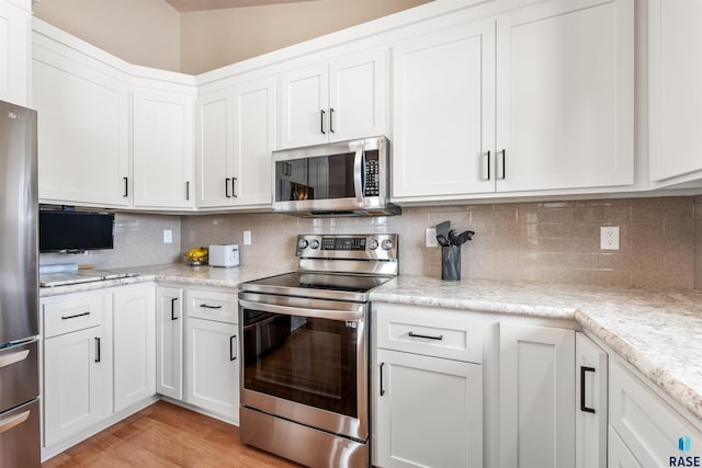 kitchen with stainless steel appliances, white cabinetry, light stone counters, and tasteful backsplash