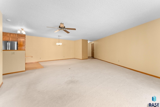 unfurnished living room featuring light carpet, a textured ceiling, baseboards, and ceiling fan with notable chandelier