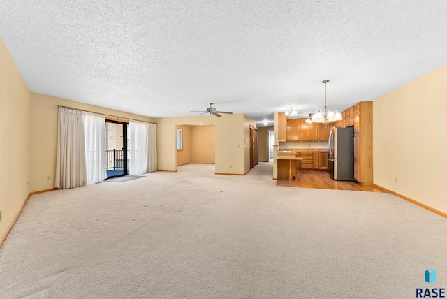 unfurnished living room with light colored carpet, a textured ceiling, baseboards, and ceiling fan with notable chandelier