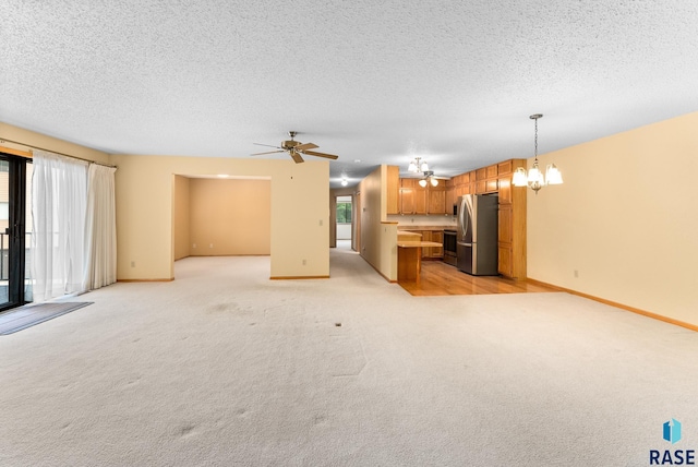 unfurnished living room with ceiling fan with notable chandelier, a textured ceiling, light colored carpet, and baseboards