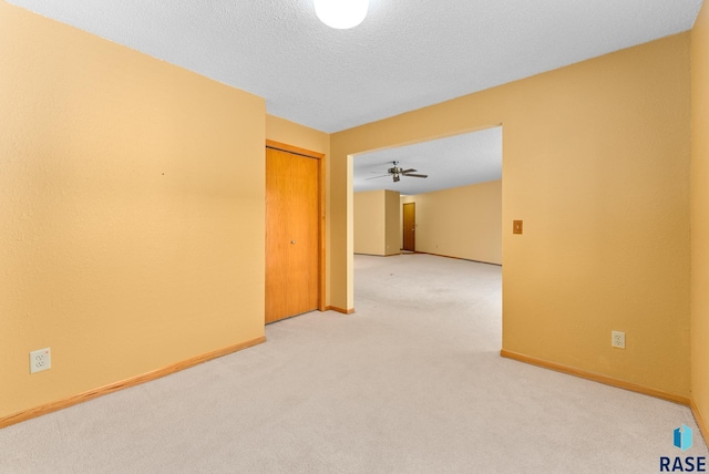 unfurnished room featuring light carpet, a ceiling fan, baseboards, and a textured ceiling