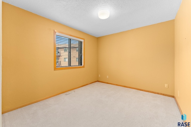 spare room with light carpet, baseboards, and a textured ceiling