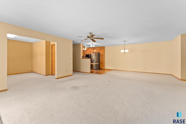 unfurnished living room with ceiling fan with notable chandelier, a textured ceiling, baseboards, and light colored carpet