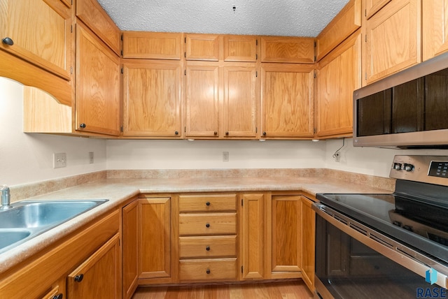 kitchen featuring brown cabinets, light countertops, appliances with stainless steel finishes, a sink, and a textured ceiling