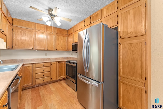 kitchen with light wood finished floors, light countertops, appliances with stainless steel finishes, a sink, and a textured ceiling