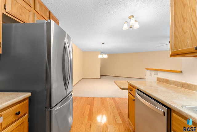 kitchen with appliances with stainless steel finishes, light countertops, hanging light fixtures, and a textured ceiling