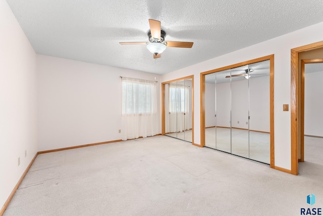 unfurnished bedroom featuring a textured ceiling, baseboards, two closets, and light colored carpet