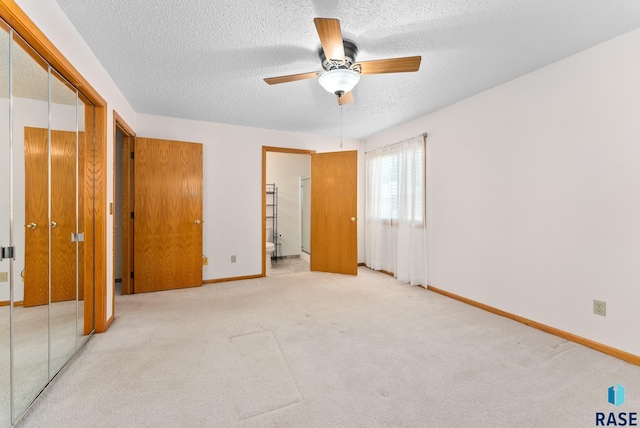 unfurnished bedroom with light carpet, ceiling fan, a textured ceiling, and baseboards