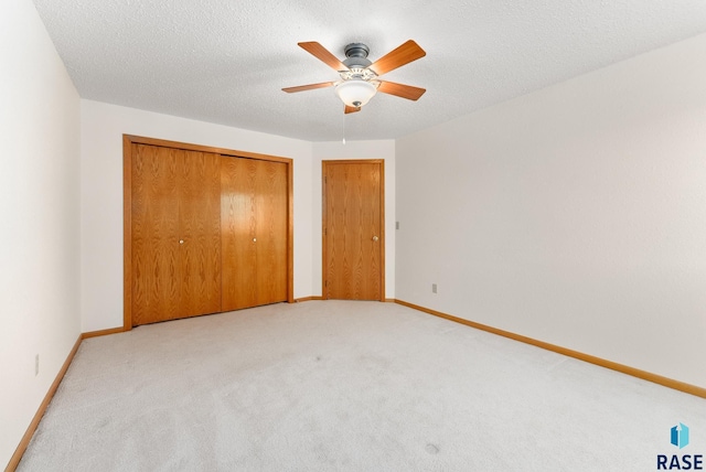 unfurnished bedroom featuring a closet, light colored carpet, a textured ceiling, and baseboards