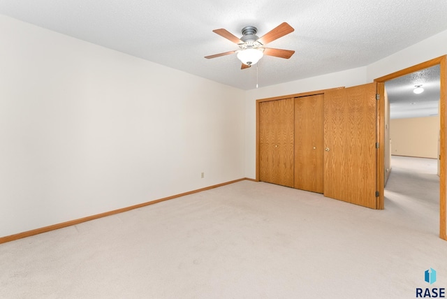 unfurnished bedroom featuring a textured ceiling, a closet, baseboards, and light colored carpet