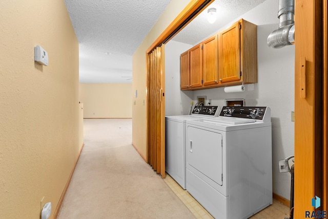 clothes washing area featuring washer and clothes dryer, cabinet space, light carpet, a textured ceiling, and baseboards