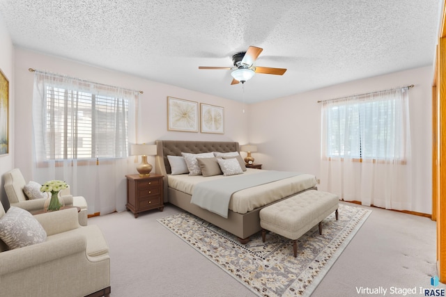 bedroom featuring a textured ceiling, ceiling fan, multiple windows, and light colored carpet