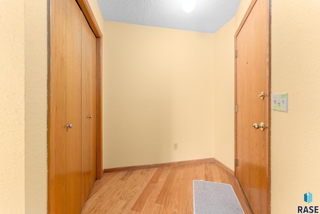 hall with light wood-style floors, baseboards, and a textured ceiling