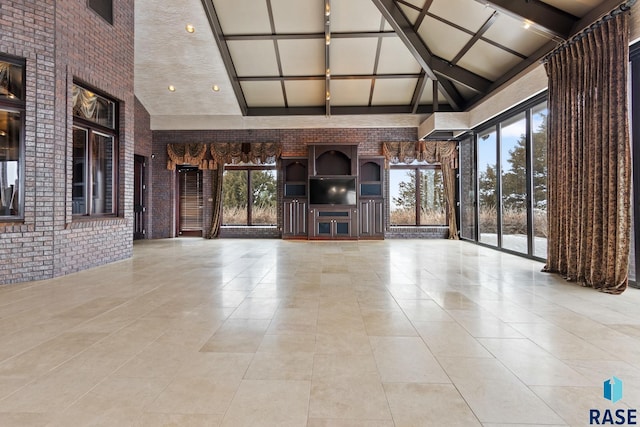 unfurnished living room with brick wall, light tile patterned flooring, high vaulted ceiling, and a wealth of natural light