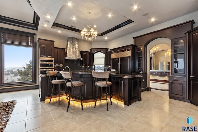 kitchen featuring pendant lighting, a center island with sink, a breakfast bar area, a raised ceiling, and paneled built in fridge