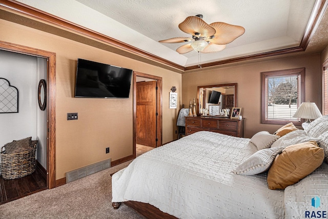 carpeted bedroom featuring a tray ceiling, visible vents, a ceiling fan, a textured ceiling, and baseboards