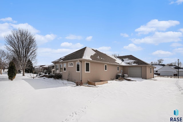 snow covered back of property with central air condition unit and a vegetable garden