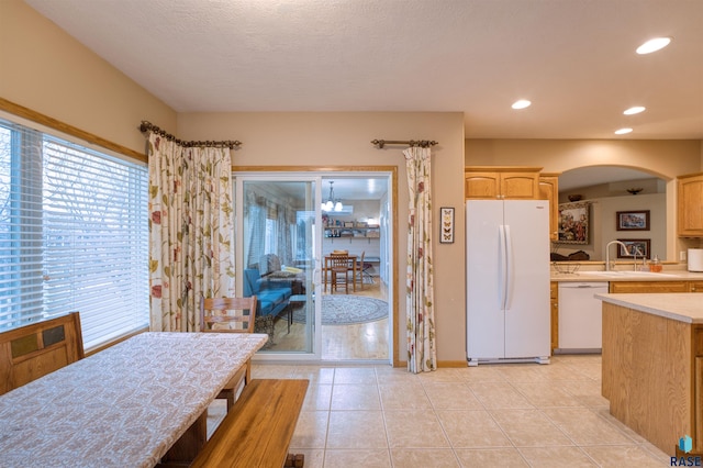 kitchen featuring white appliances, light tile patterned floors, arched walkways, light countertops, and light brown cabinets