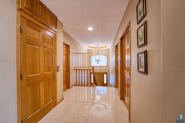 hallway featuring baseboards, marble finish floor, a textured ceiling, an upstairs landing, and a notable chandelier